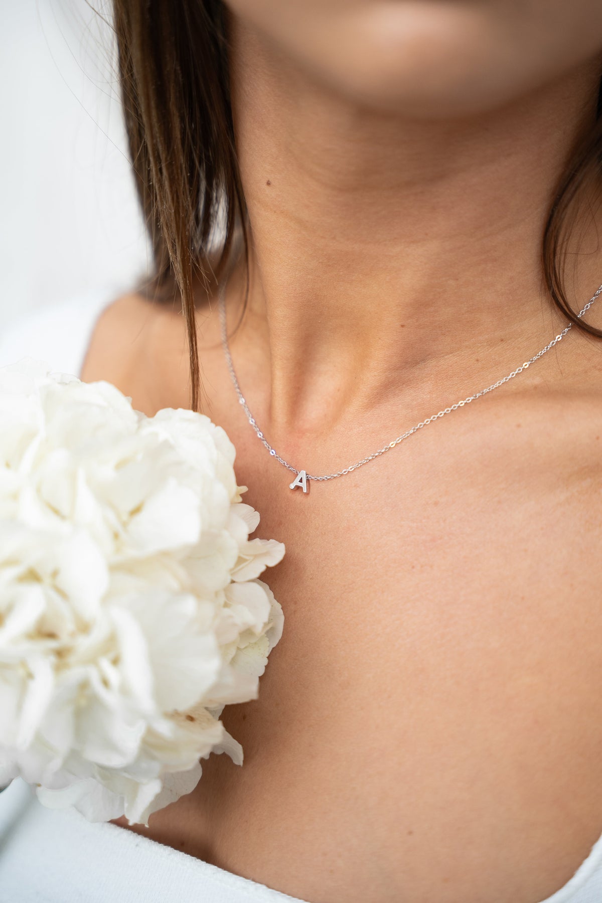 Woman with white hydrangeas wearing an Alix silver letter A breast milk necklace on her collarbone