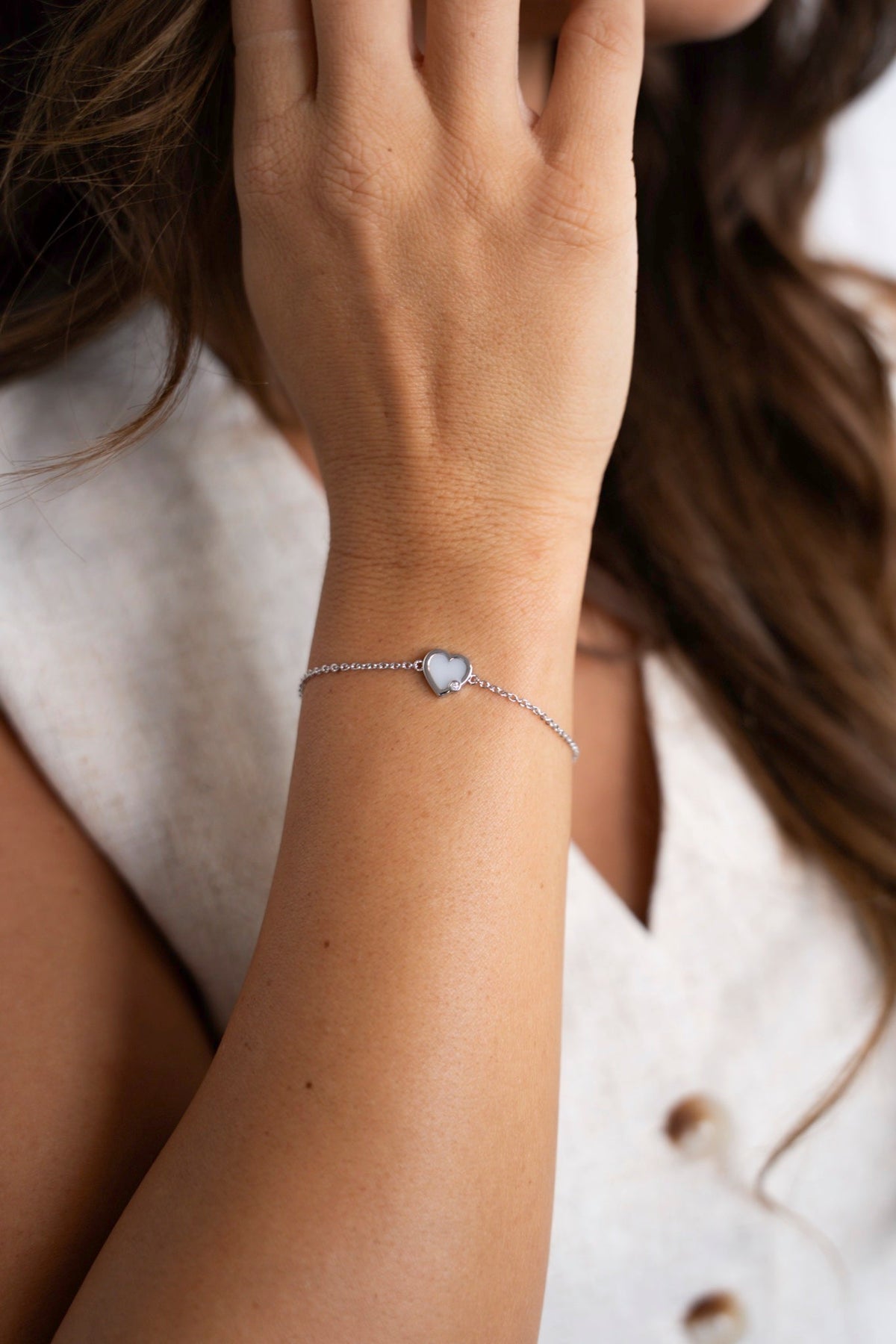 Close-up of the white gold Esmée breast milk bracelet with a heart on a fine link chain.