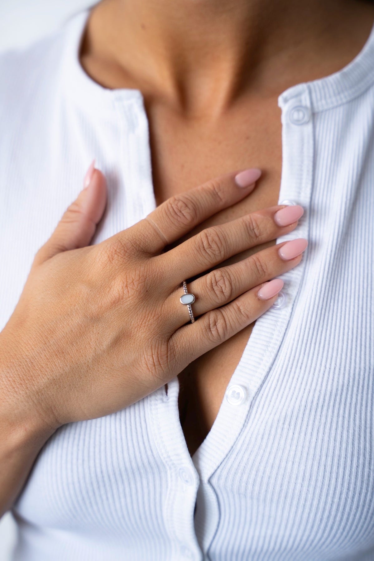 Hand on the chest wearing the Ilse breast milk ring in solid white gold, with a white ribbed cardigan.