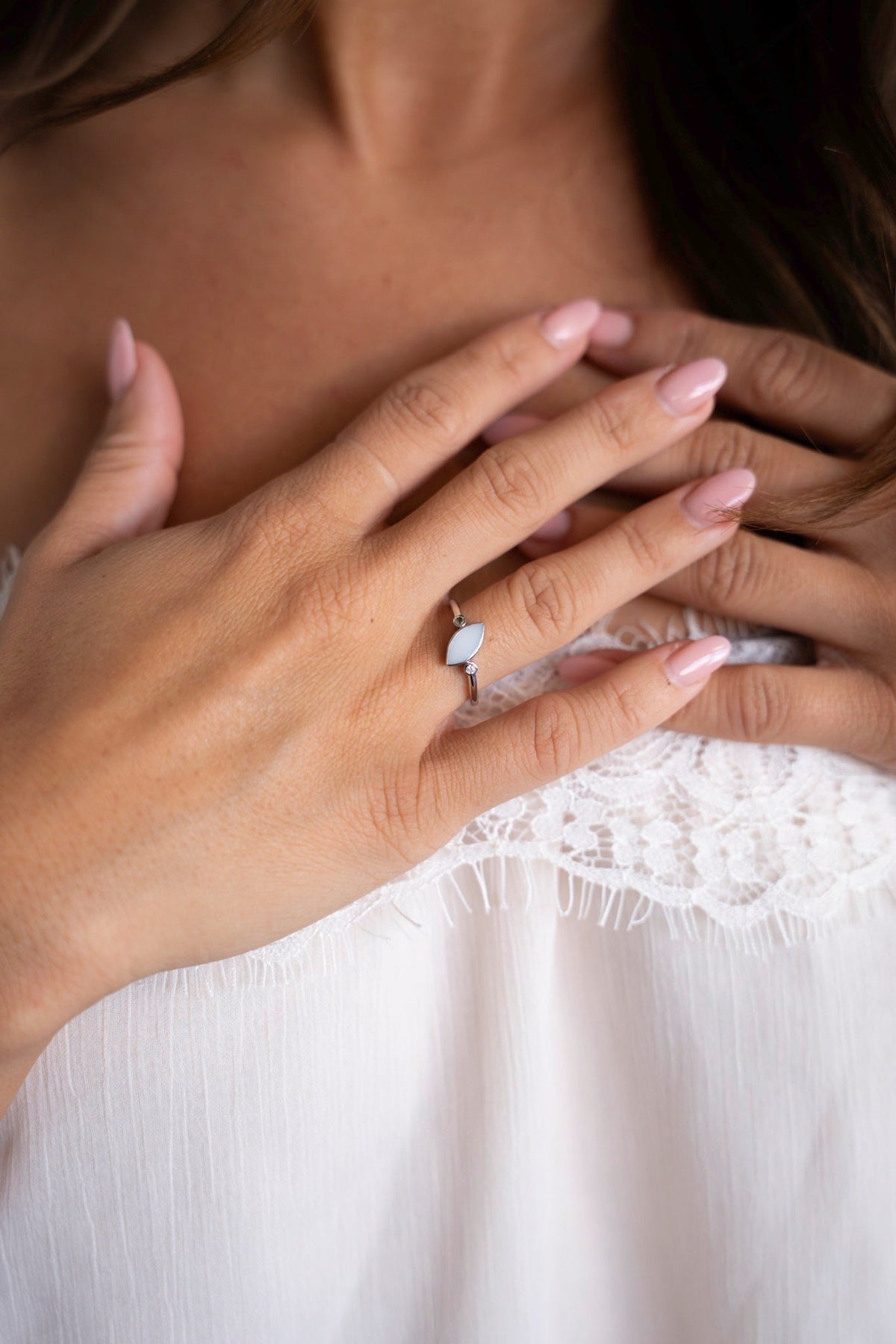 Hands on the chest with the silver Lina Duo ring, a breast milk stone with two small stones, against a white lace top.