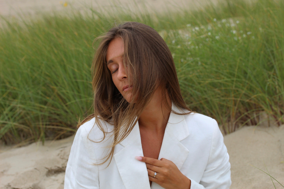 Silver Lis ring on the finger, woman with closed eyes in the dunes, hand on her chest