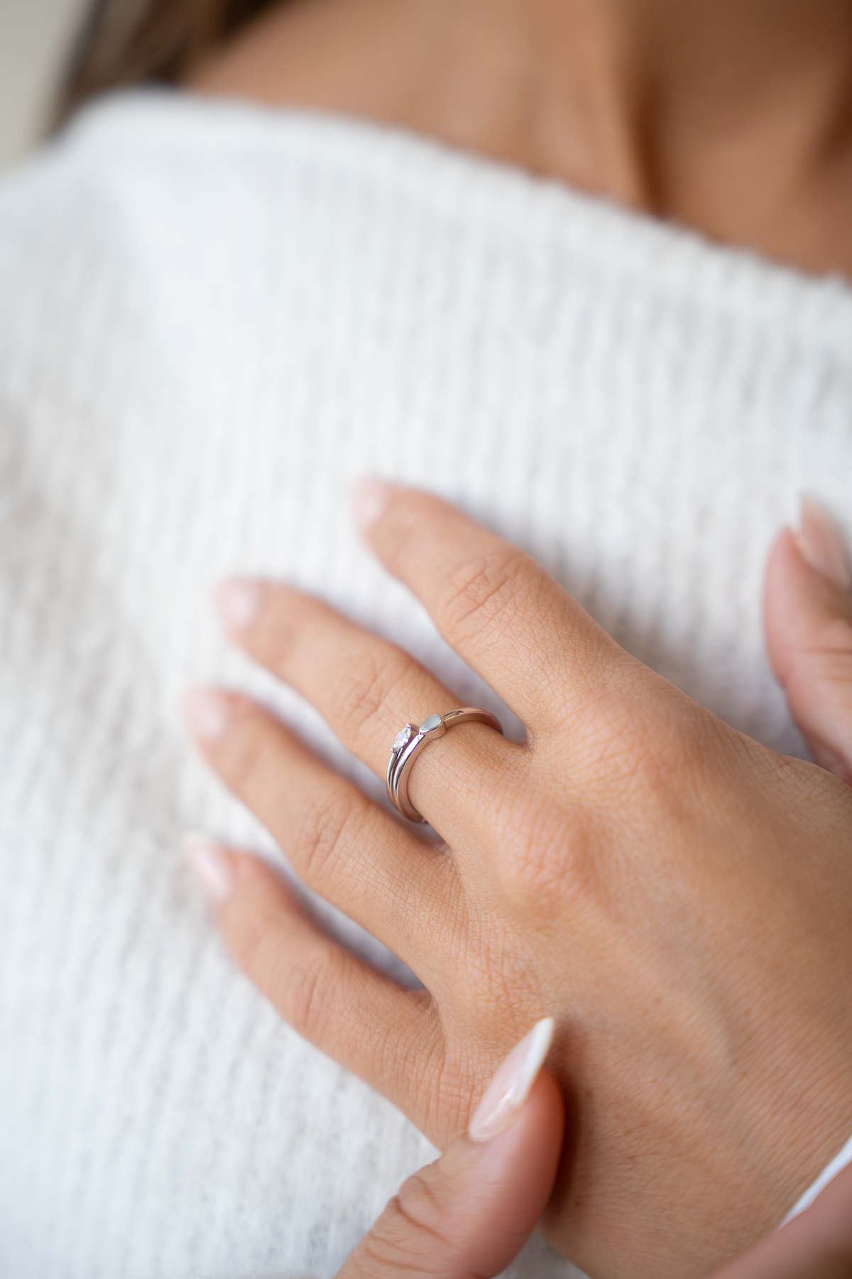 Silver Naomi open breast milk ring on the finger, hand on a white knit sweater