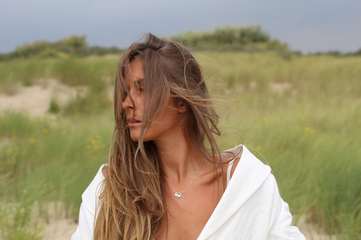 Woman with windblown hair wearing a silver-colored Trinity heart breast milk necklace in the dunes