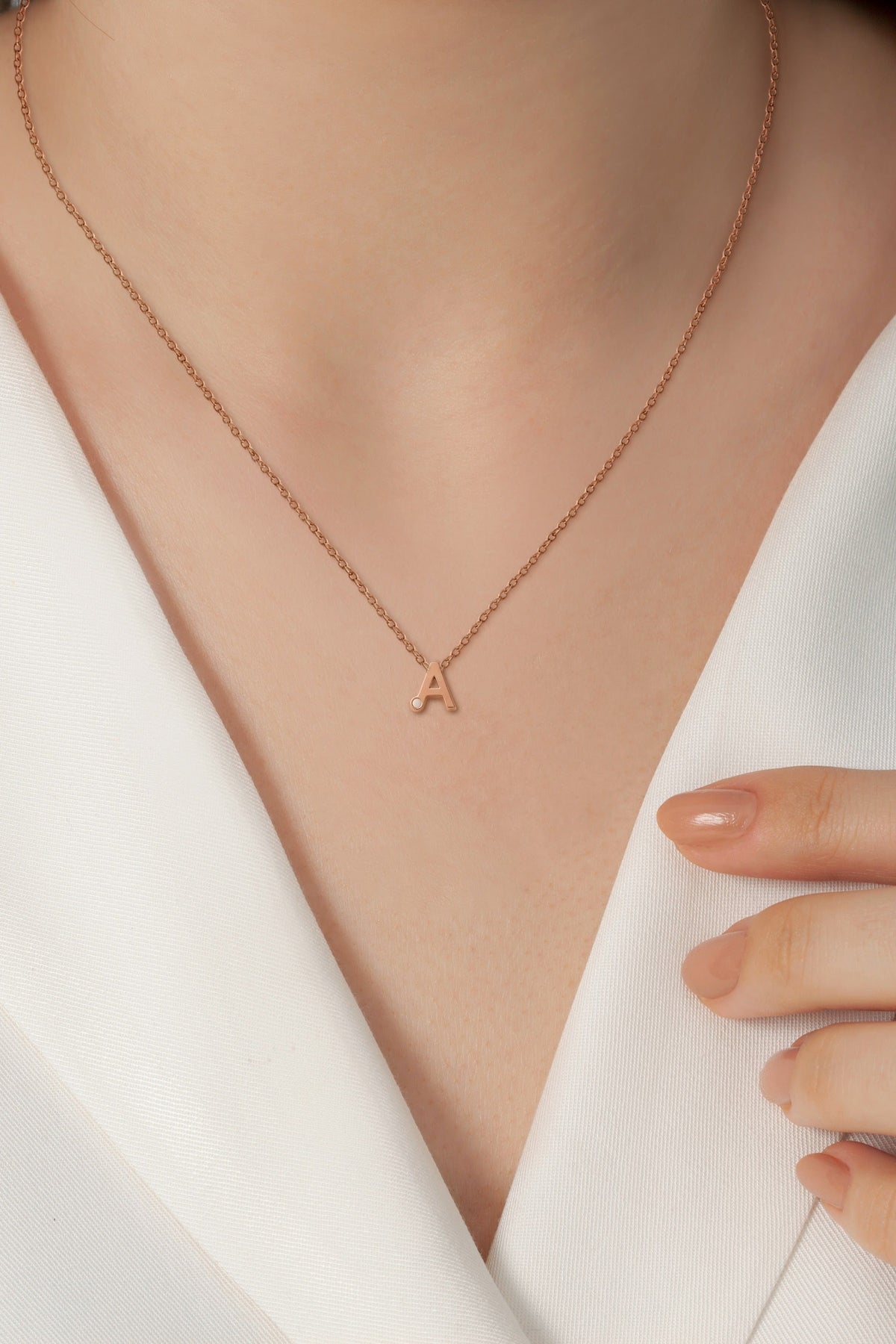 Alix rose gold letter A breast milk necklace worn on the neck with a white blazer