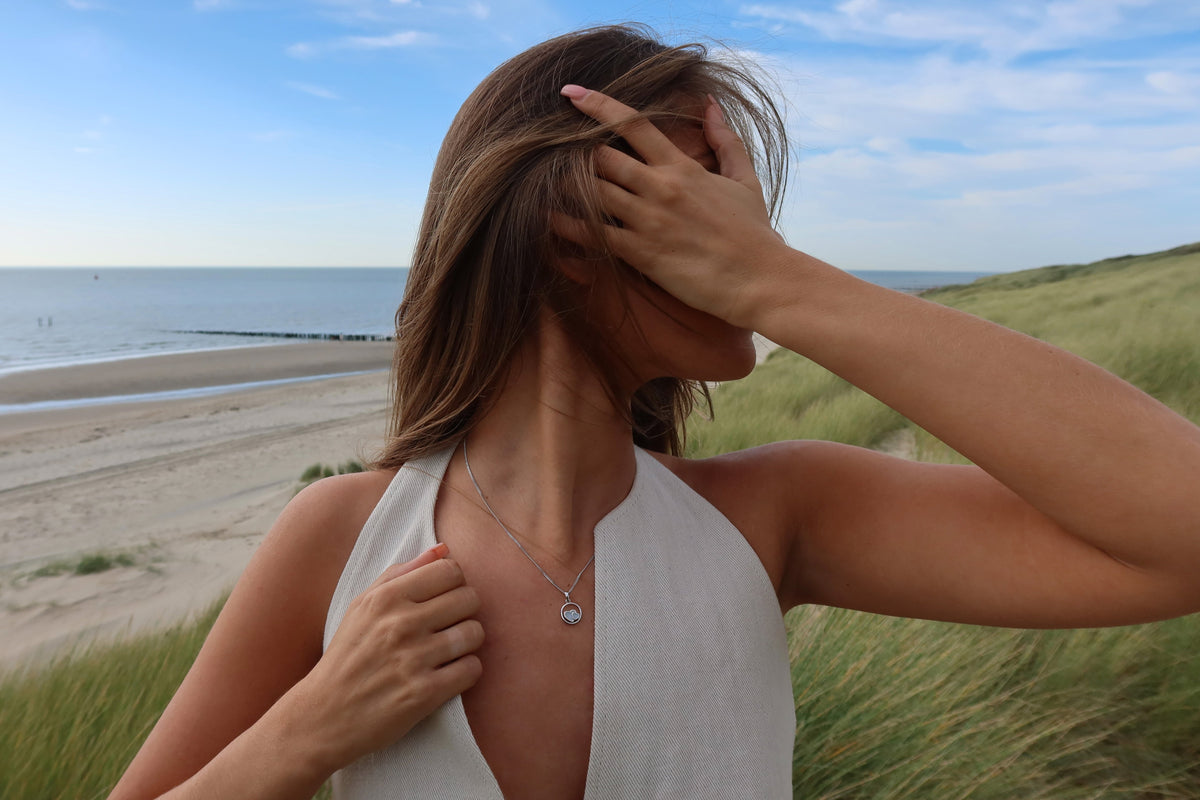 Woman by the sea wearing a silver-colored Amélie circle pendant with two breast milk hearts