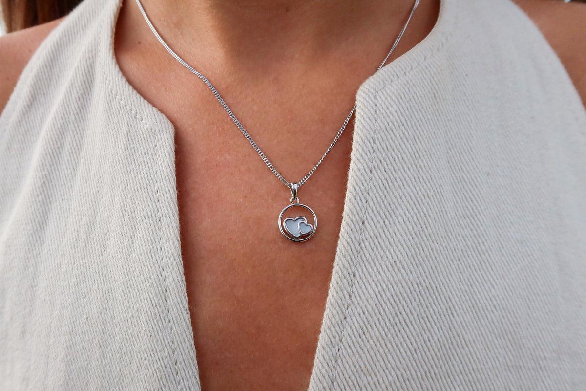 Close-up of a silver-colored Amélie circle pendant with two breast milk hearts on a curb chain