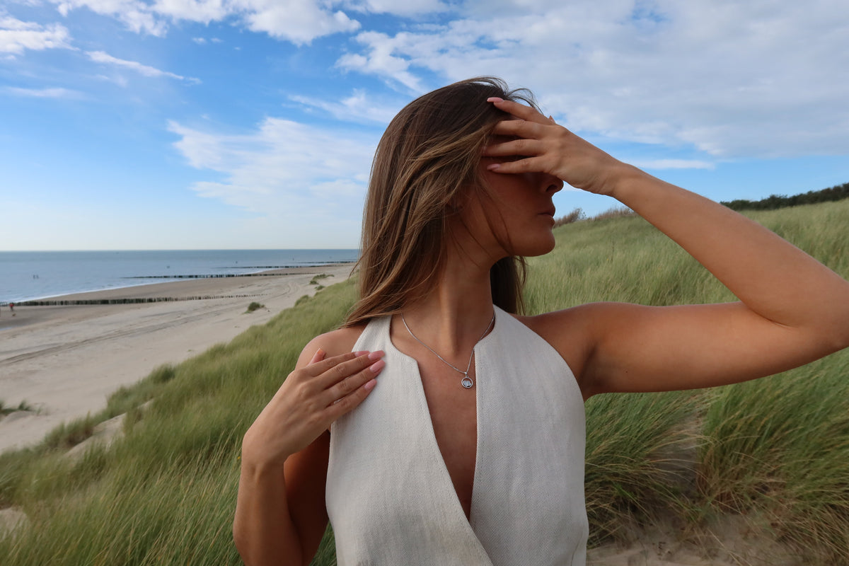 Woman in a white halter top on the dunes wearing a silver-colored Amélie two-heart breast milk pendant