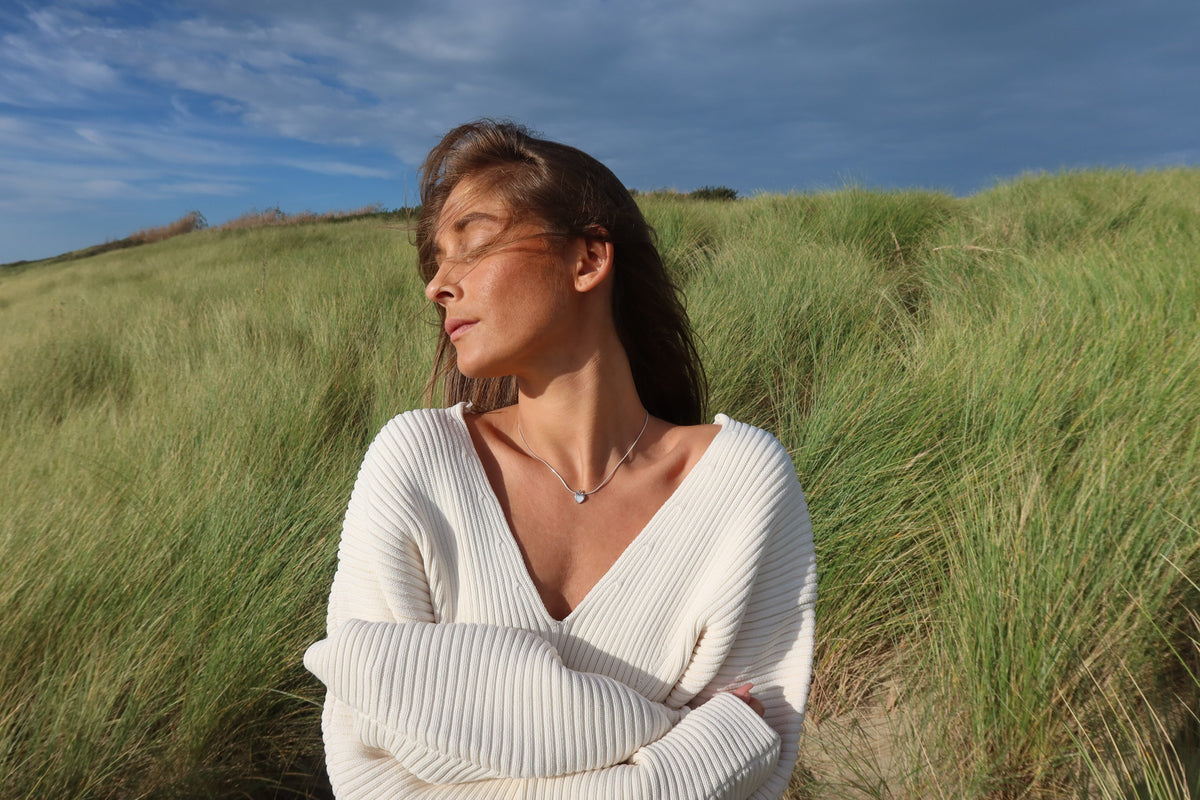 Woman in a white sweater with crossed arms wearing a silver-colored Amore heart breast milk pendant