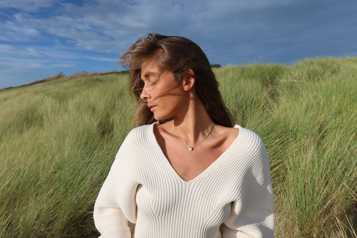 Woman in the dunes wearing the small silver Amore heart breast milk pendant on a fine chain