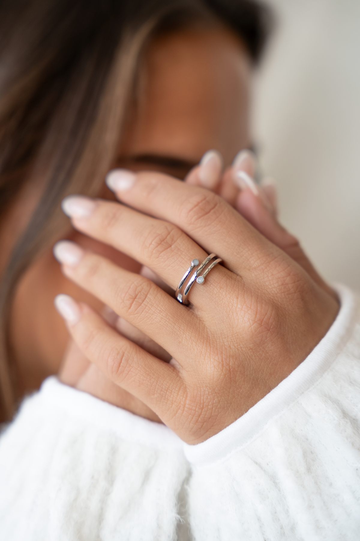 Woman covering her face with her hands, silver Aurore breast milk ring with two milk stones visible