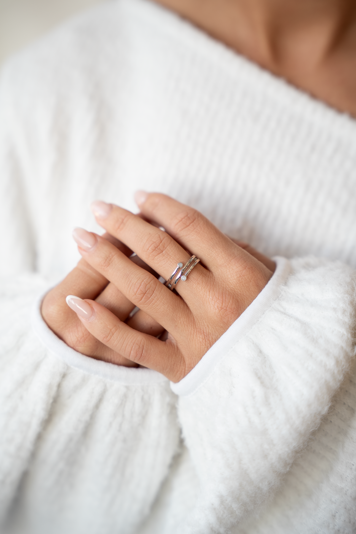 Folded hands against a white sweater showing the silver Aurore spiral breast milk ring