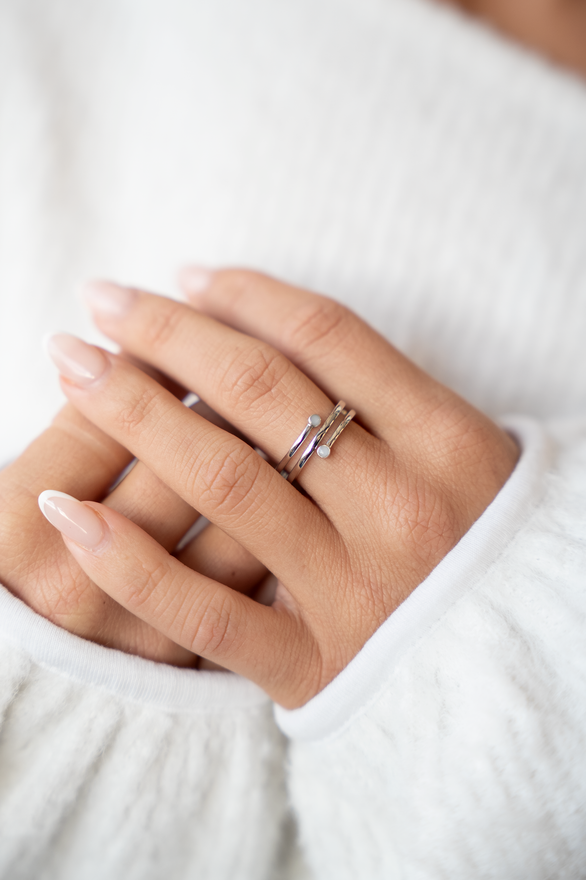 Close-up of folded hands wearing the silver Aurore breast milk ring with two small milk stones