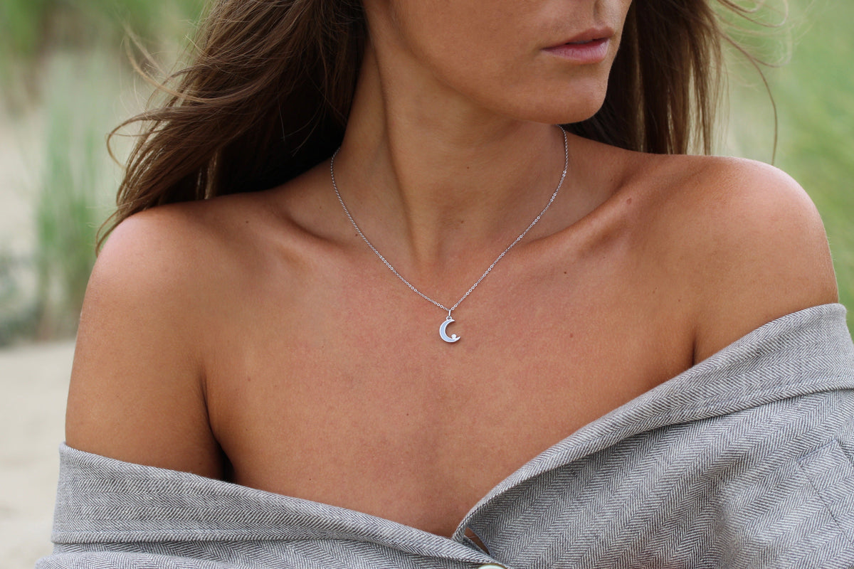 Close-up of the silver Ayla crescent moon breast milk pendant on a fine chain at the collarbone