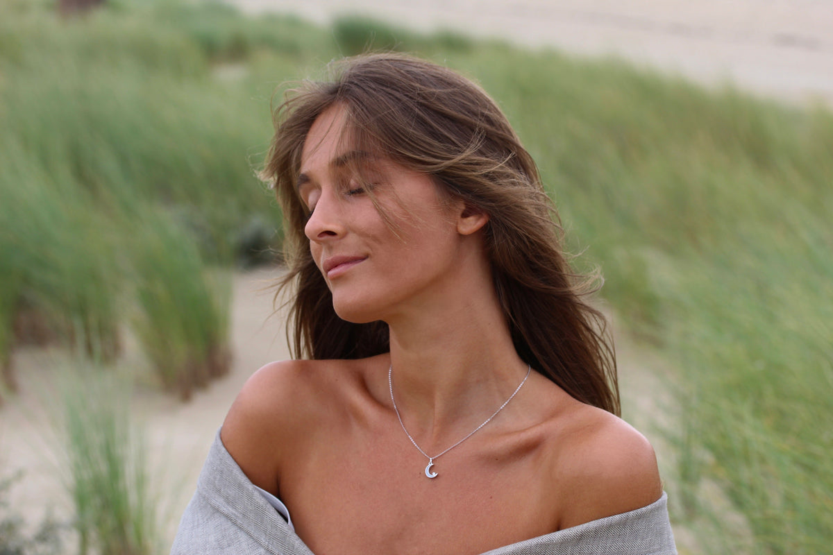 Woman with closed eyes in the dunes wearing the small silver Ayla moon breast milk pendant