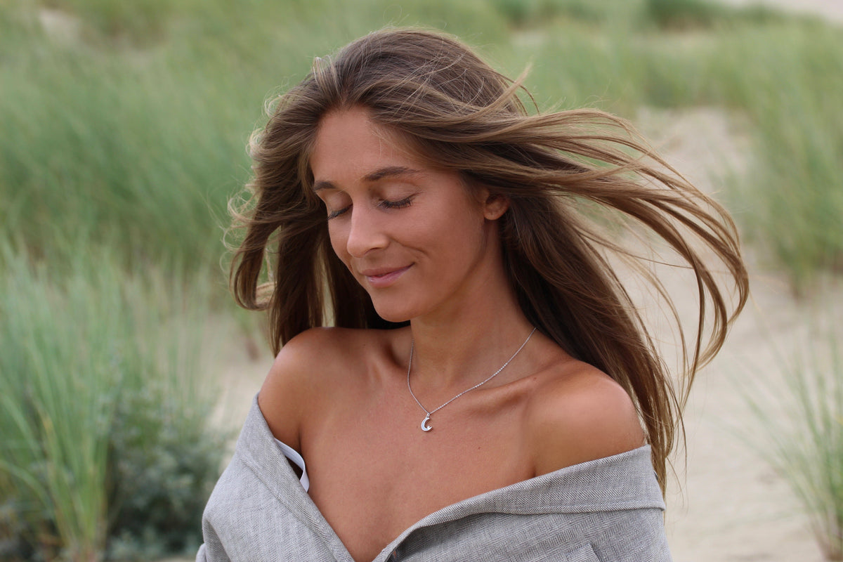 Smiling woman with windblown hair wearing the silver Ayla crescent moon breast milk pendant