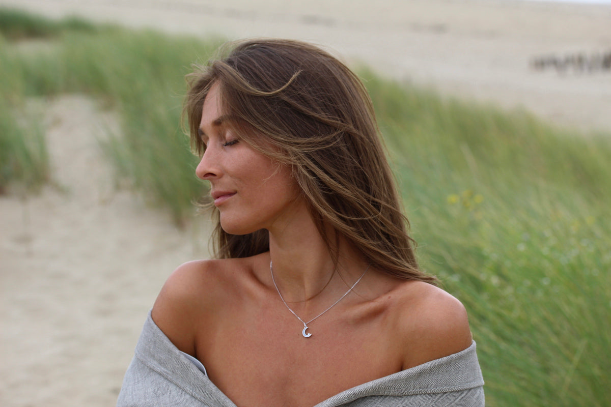 Woman in a gray wrap in the dunes wearing a silver-colored Ayla crescent moon breast milk pendant