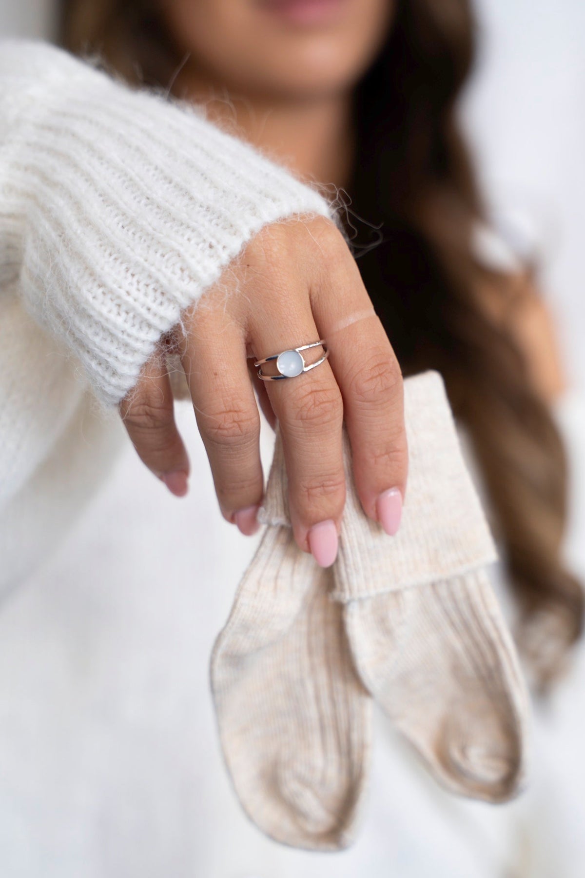 Silver Bea ring with a round breast milk stone, worn by a woman in a white sweater holding baby socks.