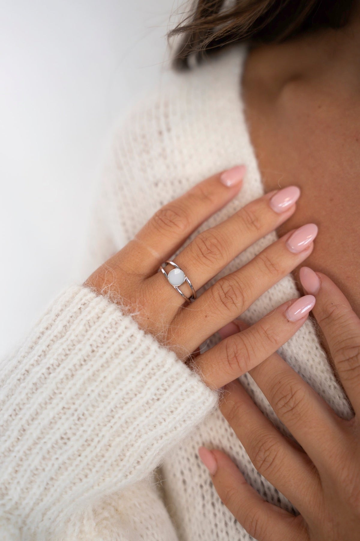Close-up of the Bea ring in 925 sterling silver with a round breast milk stone, hand resting on a white knit sweater.