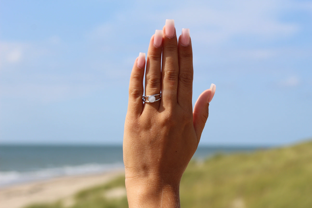 Raised hand against the sea and sky showing the silver Bea split-band breast milk ring
