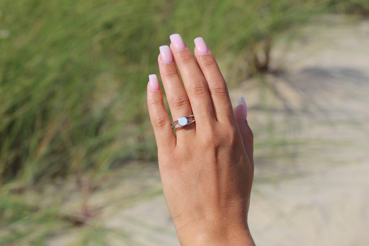 Hand in front of dune grass showing the silver Bea breast milk ring with round milk stone