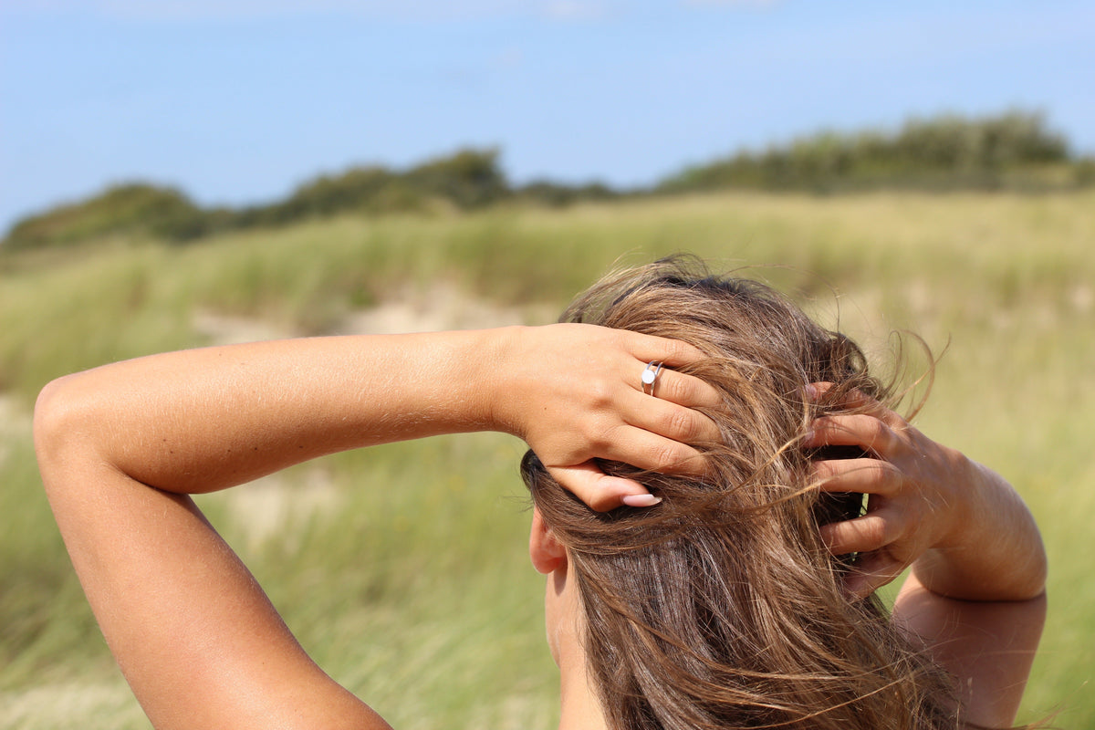 Woman seen from behind with hands in her hair wearing the silver-tone Bea breast milk ring