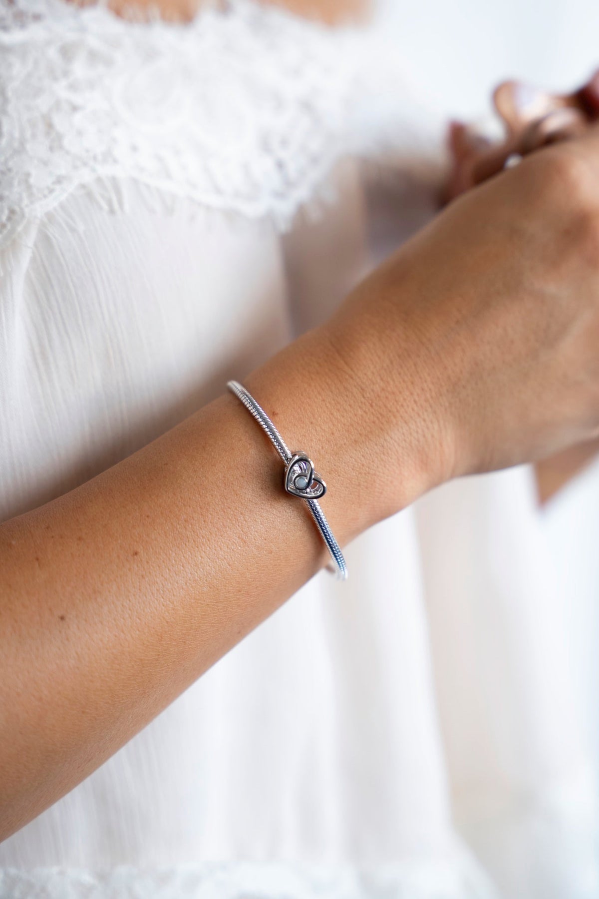 Heart-shaped silver Bente charm with breast milk on a charm bracelet around the wrist.