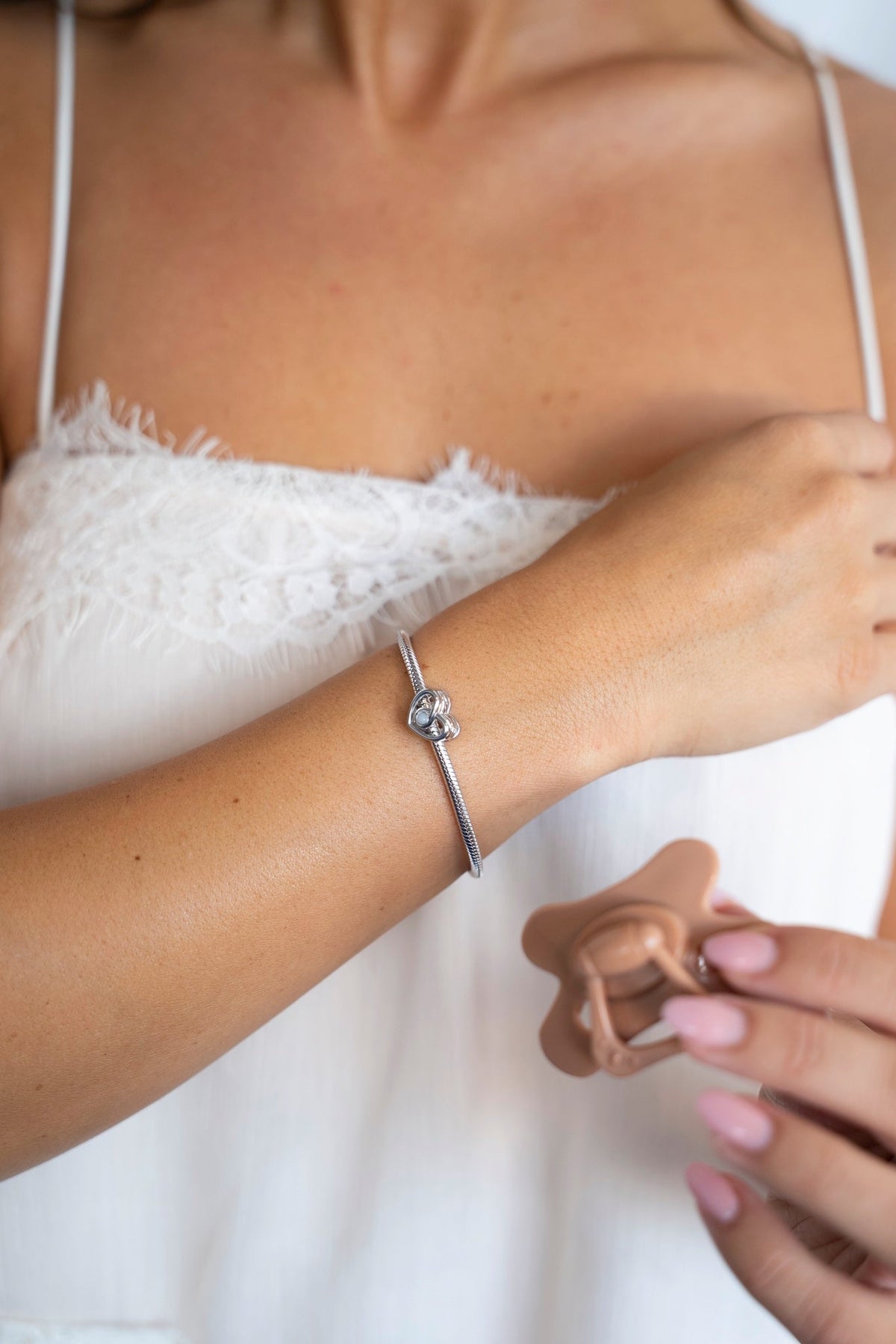 Bente breast milk charm in 925 sterling silver on the wrist while a hand holds a pacifier.