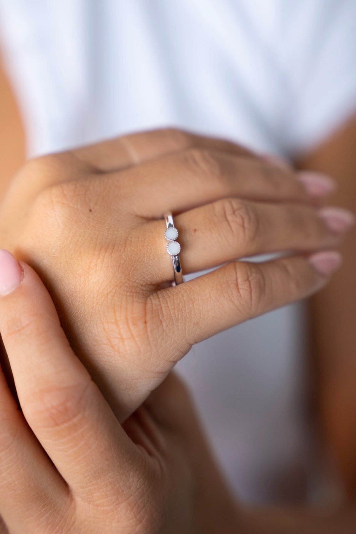 White gold Bo ring with two small breast milk stones side by side, worn on the ring finger.