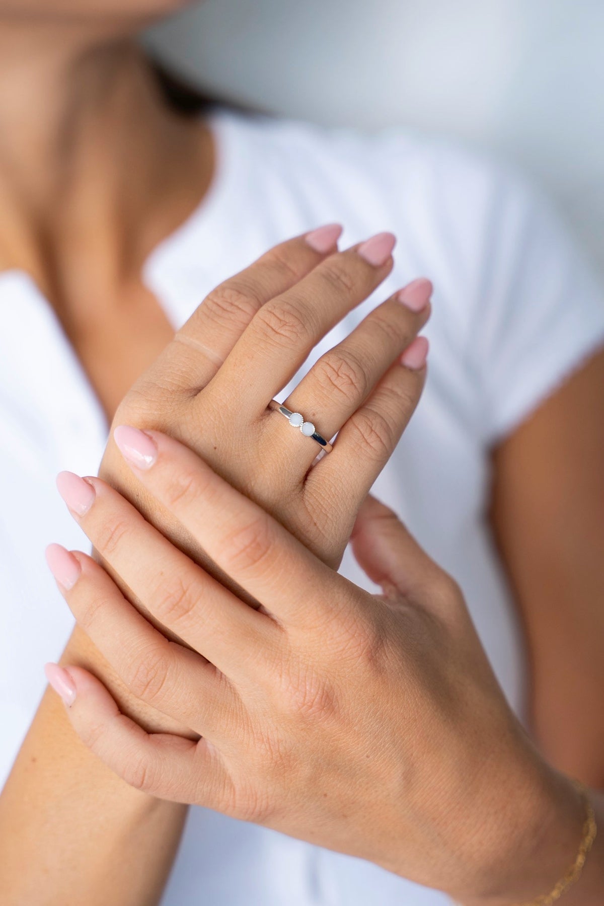 Bo breast milk ring in solid white gold on a hand resting on the other hand, against a white shirt.