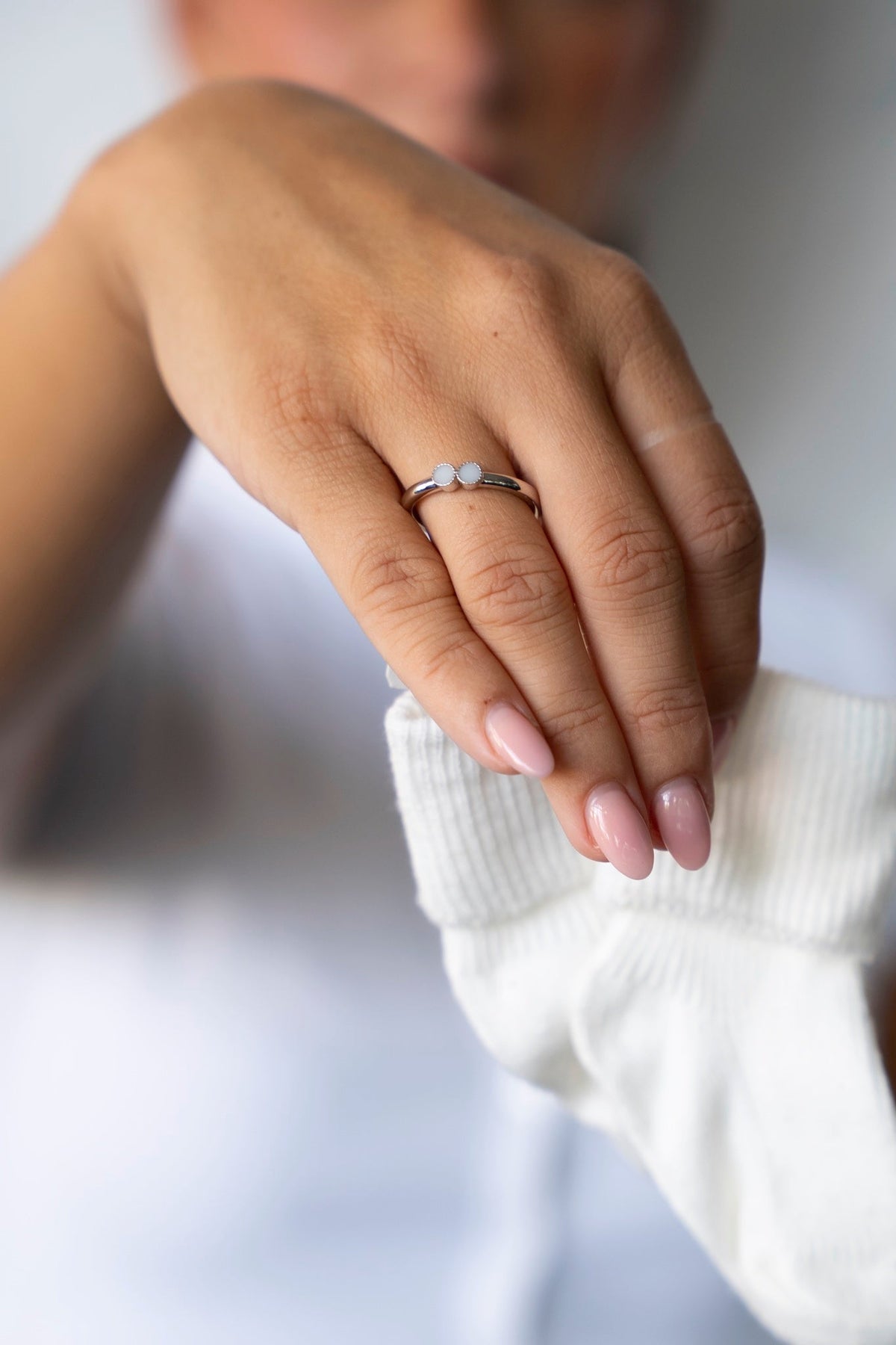 Hand wearing the white gold Bo breast milk ring, holding a white baby sock.