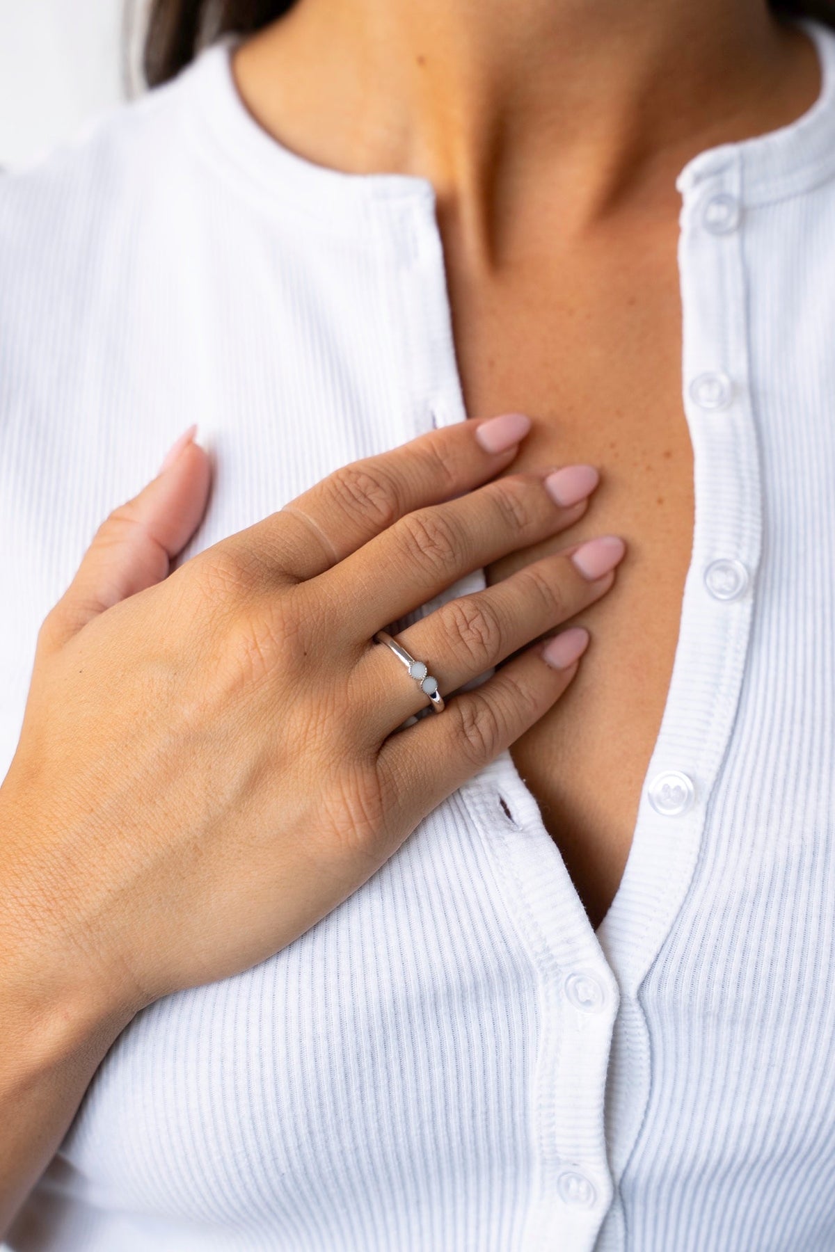 Woman in a white ribbed cardigan with her hand on her chest, wearing the Bo ring in solid white gold.