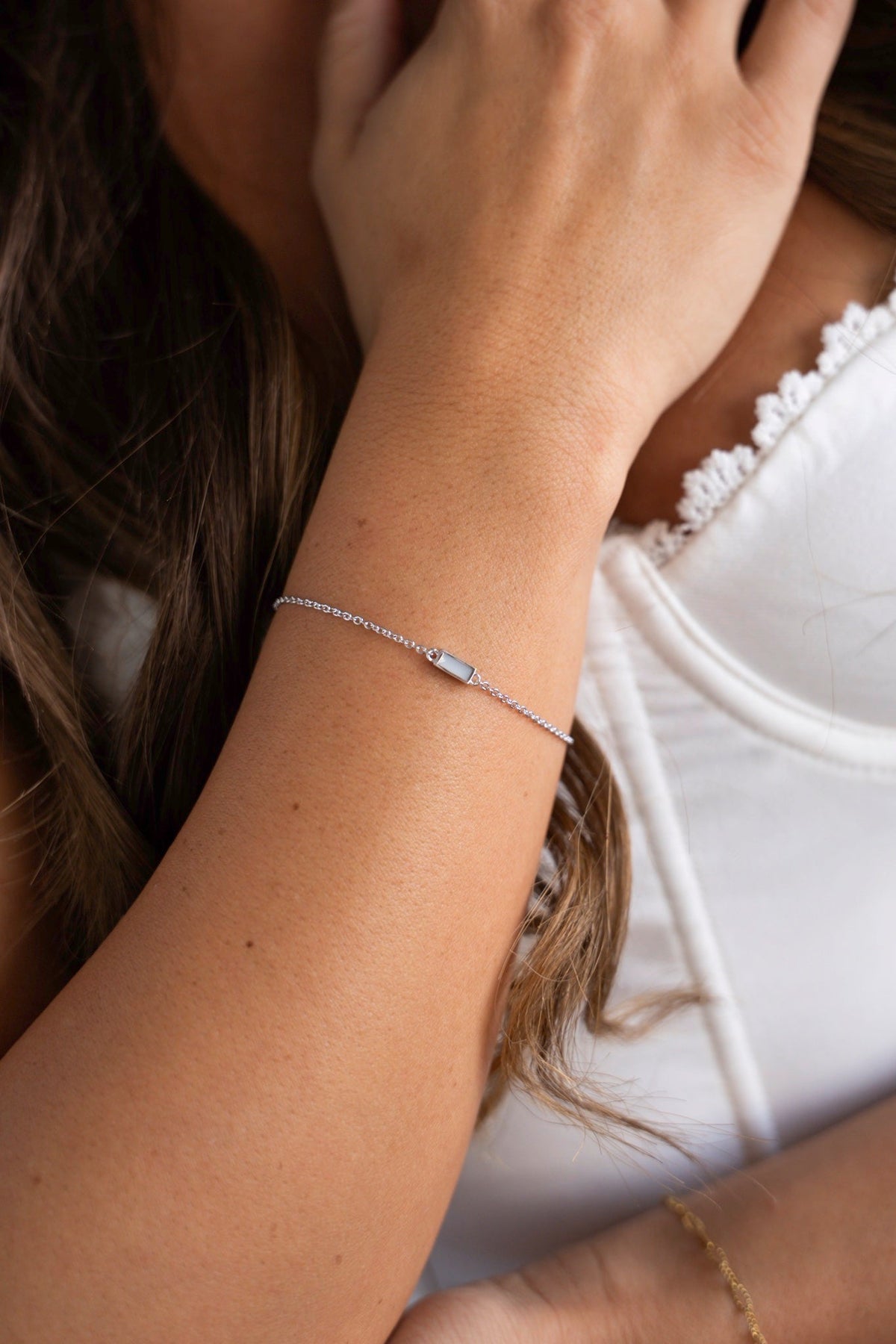 Britt bracelet in white gold with a rectangular breast milk stone on the wrist, the hand in the hair.