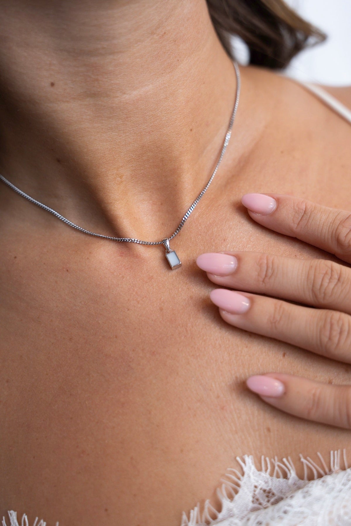 Britt breast milk pendant in 925 sterling silver resting on the collarbone, one hand on the chest.