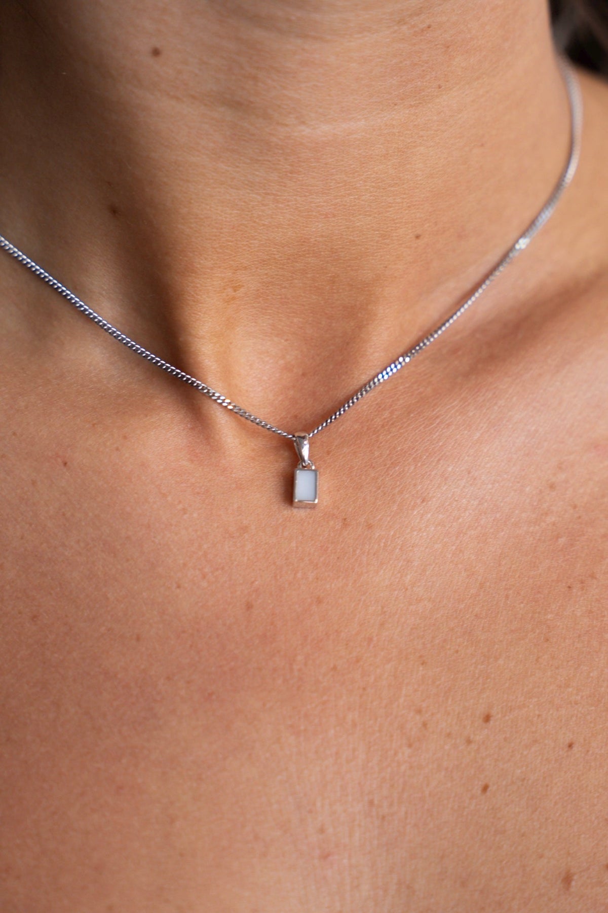 Close-up of the white gold Britt pendant with a rectangular breast milk stone at the neck.