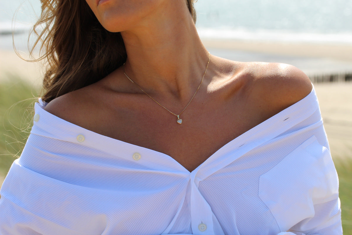 Close-up of the small silver Cara heart breast milk pendant with an off-shoulder white shirt