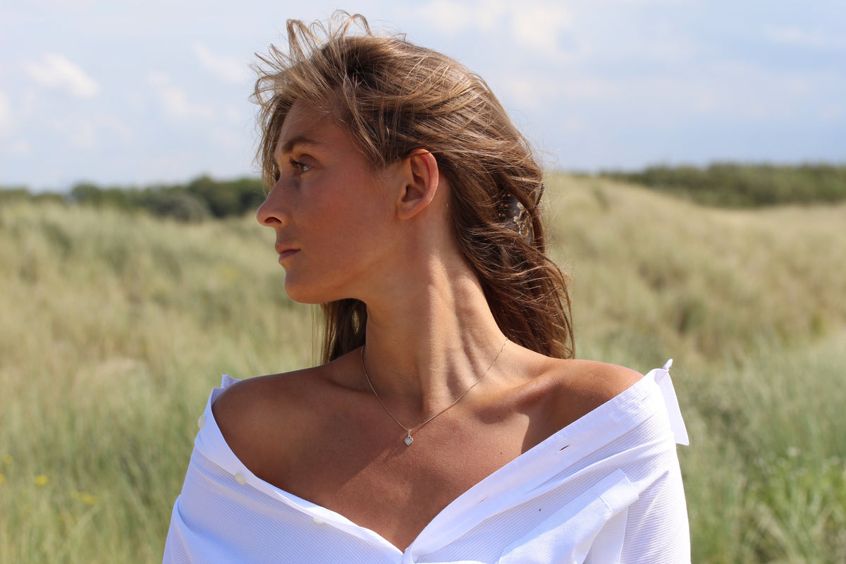 Woman looking sideways in the dunes wearing the small silver Cara heart breast milk pendant