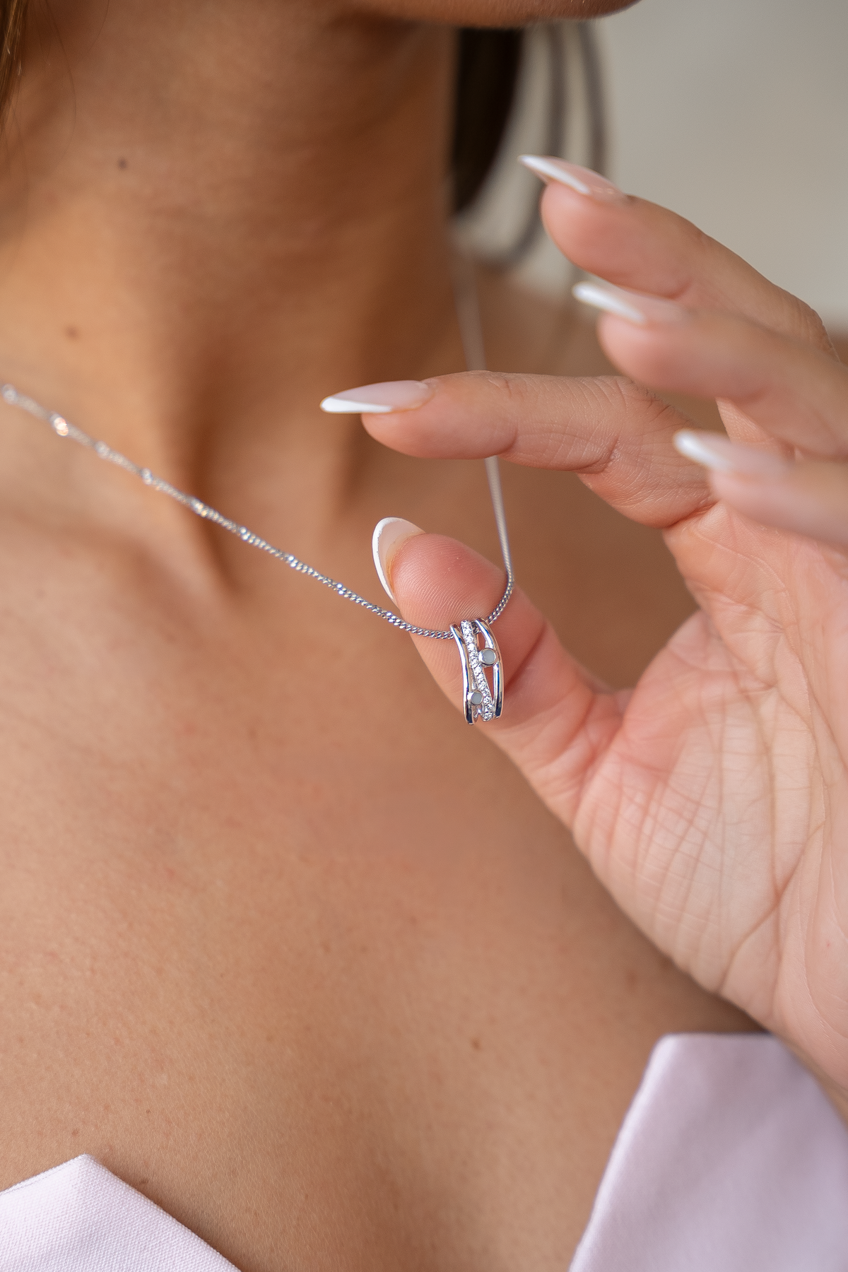 Fingertip holding the silver Charlotte pendant with clear stones and breast milk stones on a fine chain