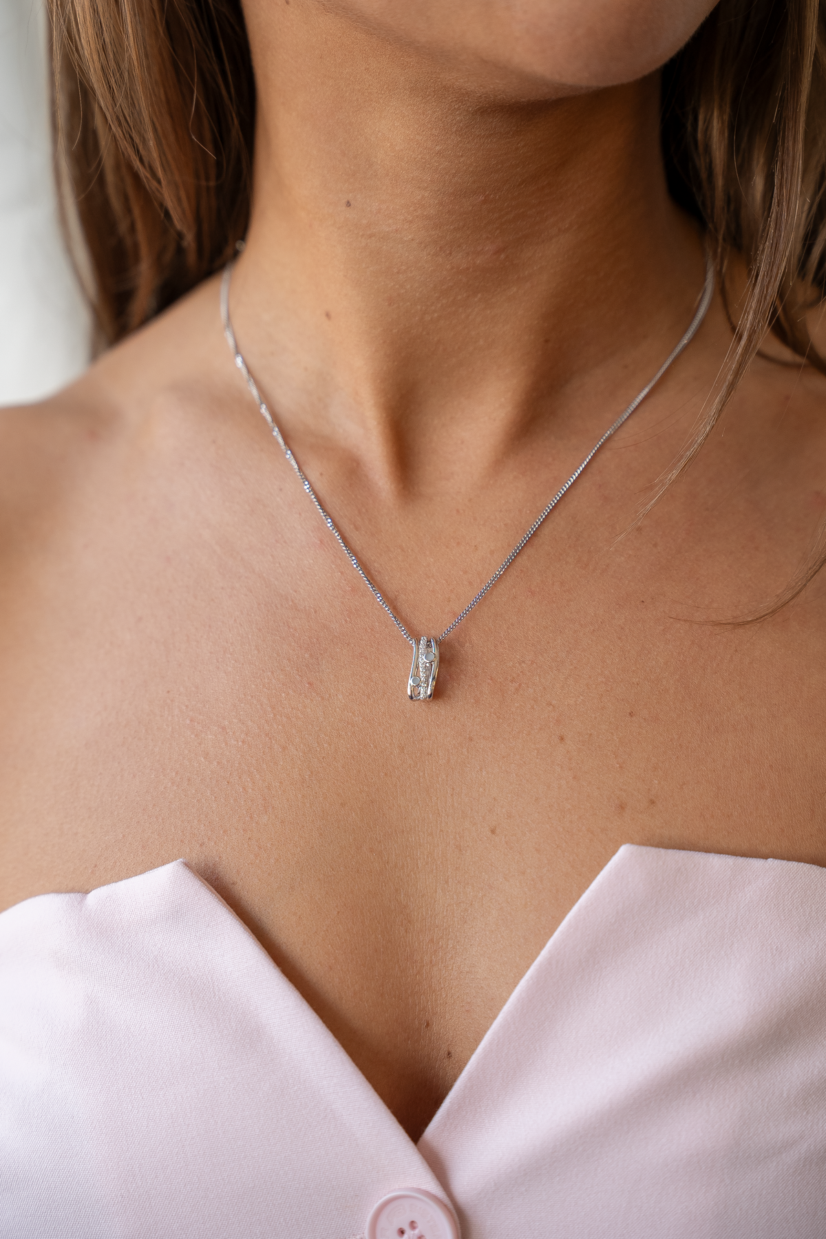 Silver Charlotte breast milk pendant on a fine chain, worn with a pale pink strapless top