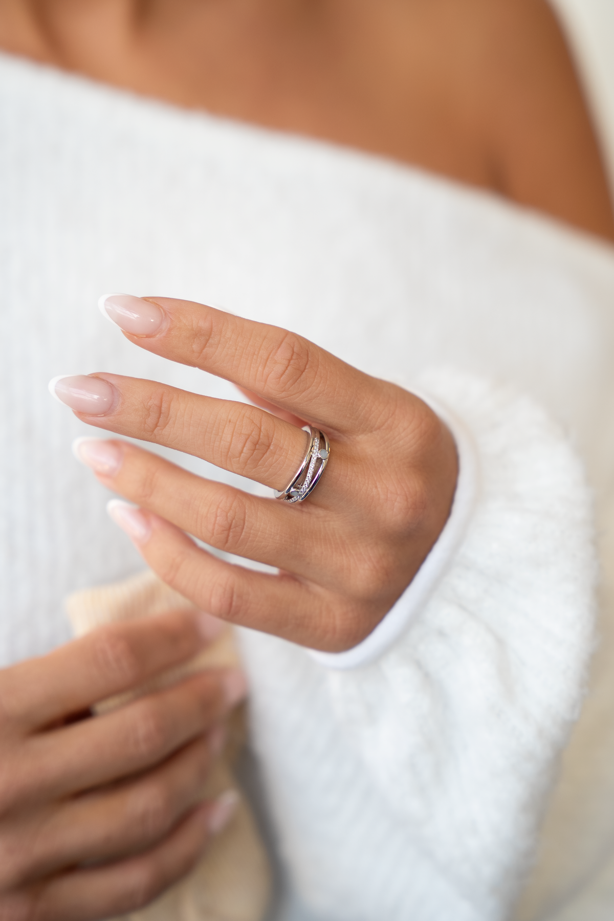 Silver Charlotte breast milk ring with two round milk stones worn on the ring finger against a white sweater