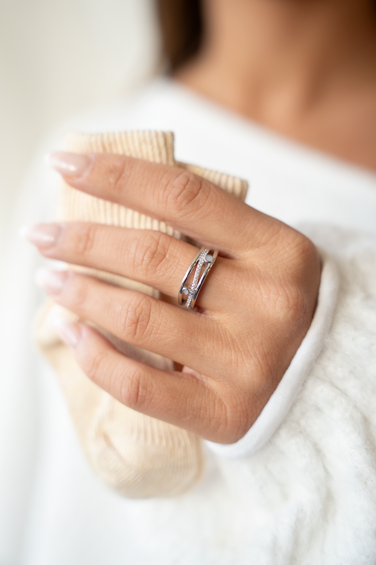 Hand holding a beige knit wearing the silver Charlotte breast milk ring with clear stones and two milk stones