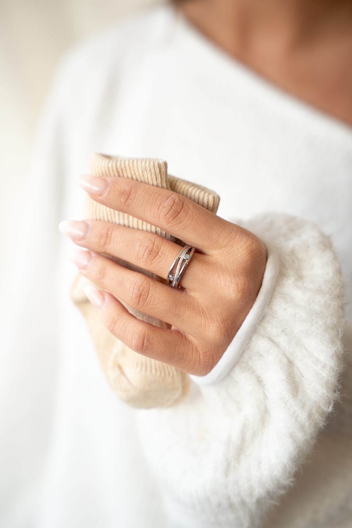 Silver Charlotte breast milk ring worn on a hand holding a beige knit, white sweater sleeve
