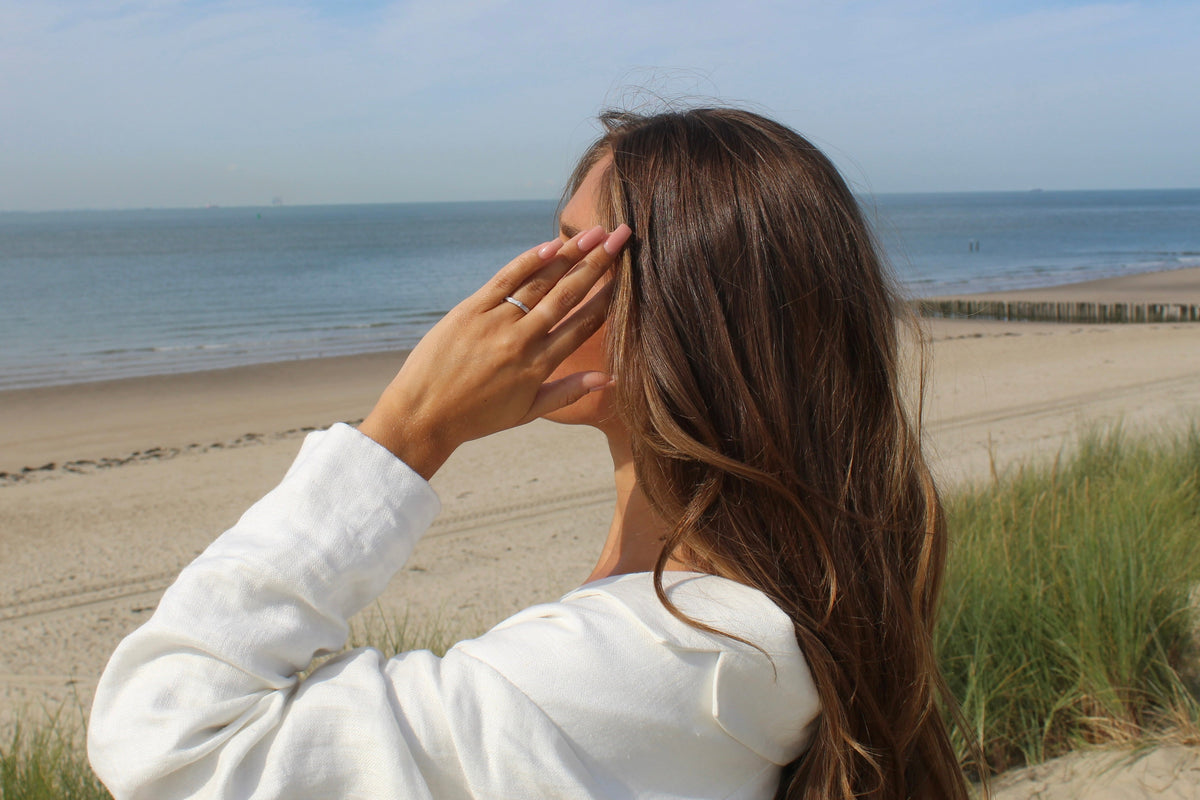 Woman on the beach touching her hair, wearing the silver Cinderella breast milk ring