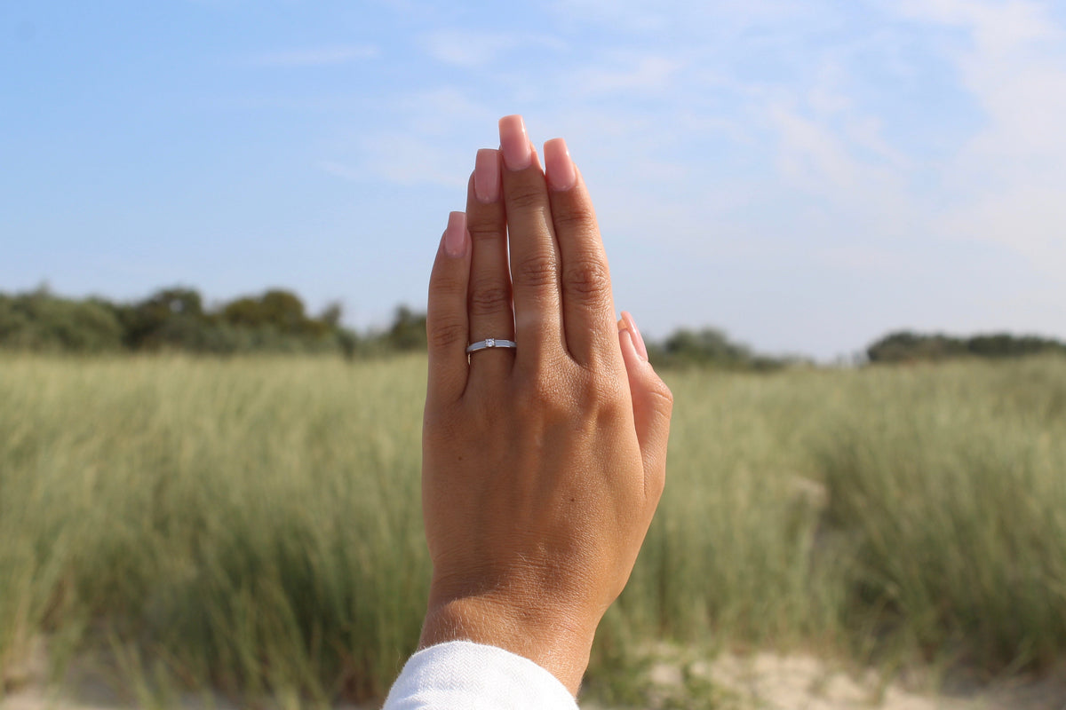 Back of a hand against dune grass and sky wearing the slim silver Cinderella breast milk ring