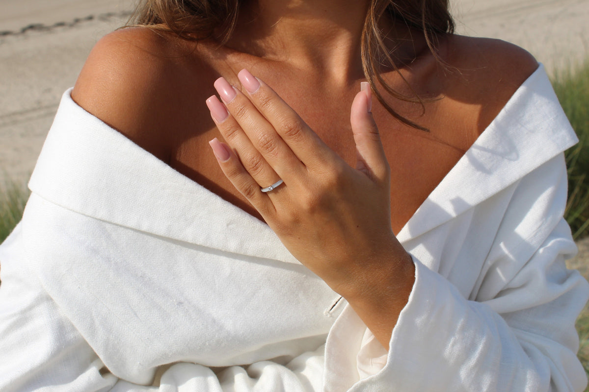 Hand resting on the chest over a white linen shirt, wearing the silver Cinderella breast milk ring