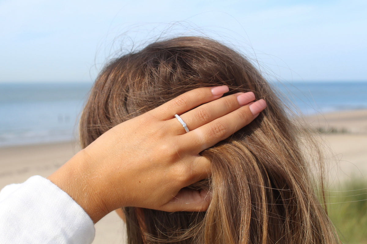Hand in long brown hair on the beach wearing the silver Cinderella breast milk ring with a center stone
