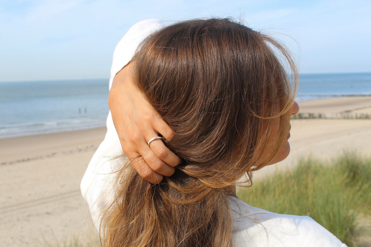 Hand gathering hair at the beach, wearing the silver Cinderella breast milk ring