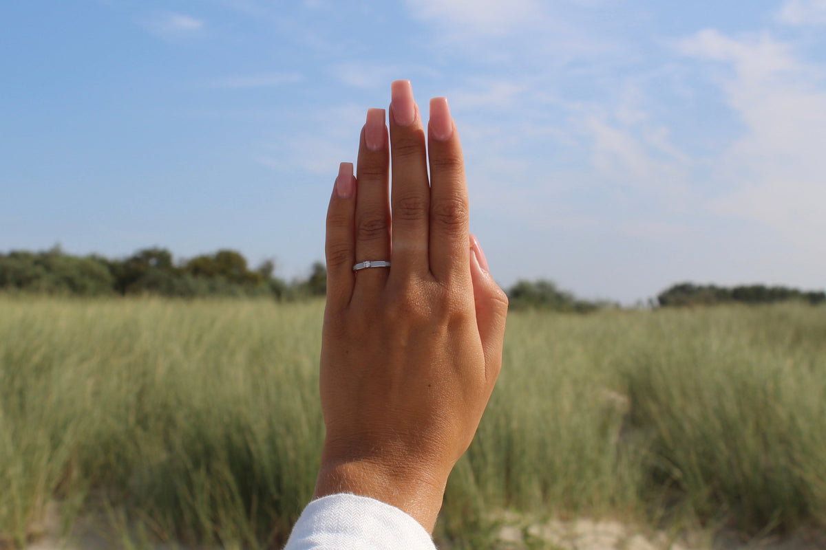 Raised hand in front of dune grass wearing the silver Cinderella breast milk ring with white milk inlay