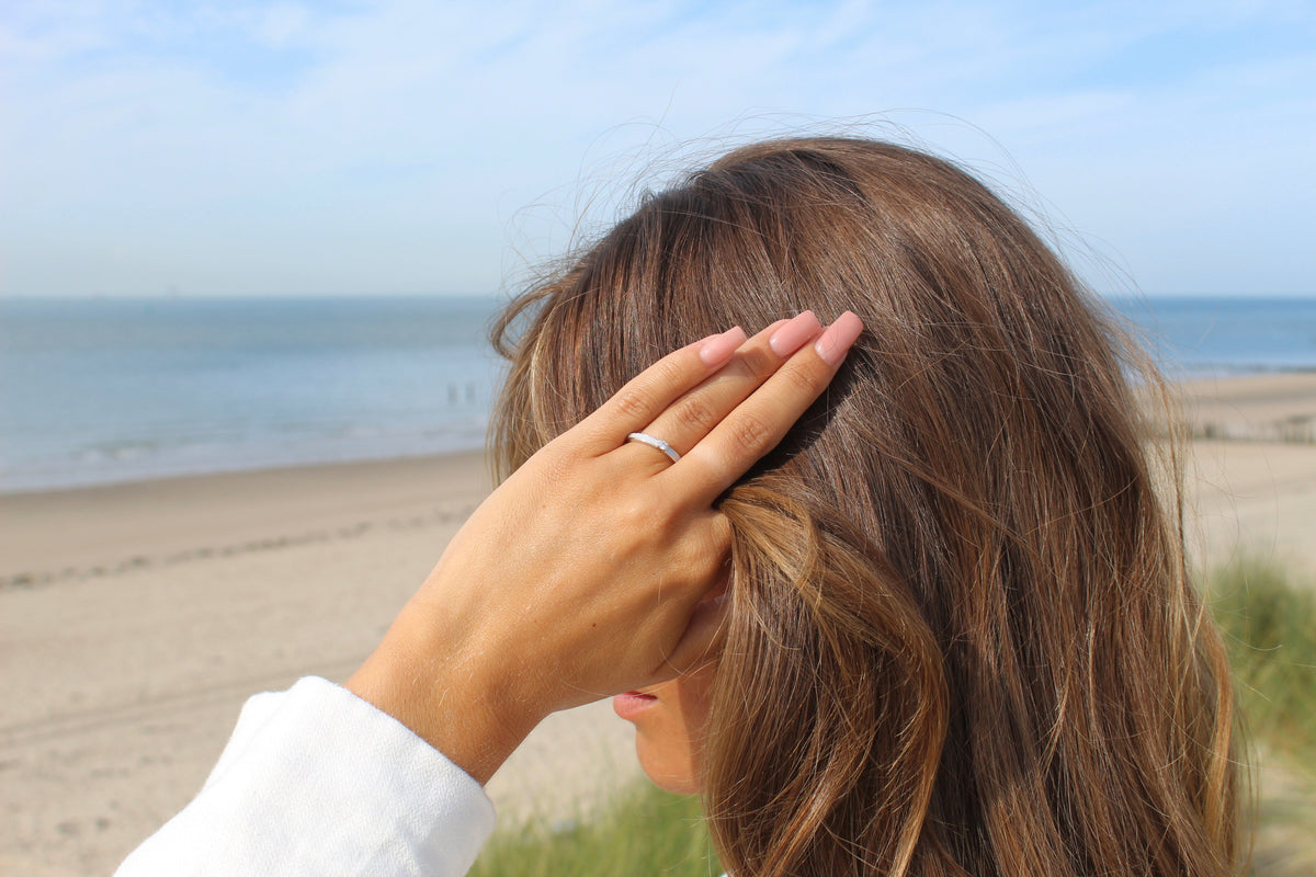 Hand tucking hair behind the ear at the beach, wearing the silver Cinderella breast milk ring