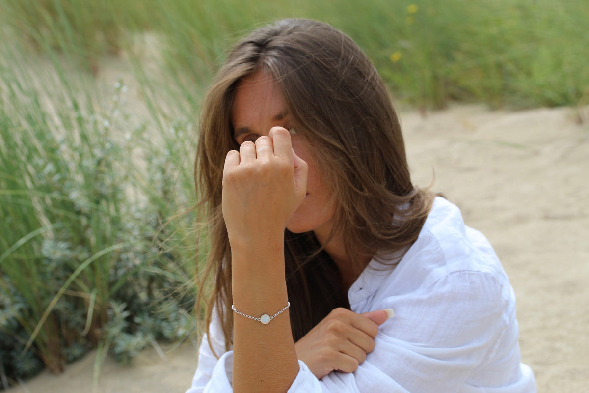 Woman in a white shirt on a beach wearing the silver Circle of Life breast milk bracelet