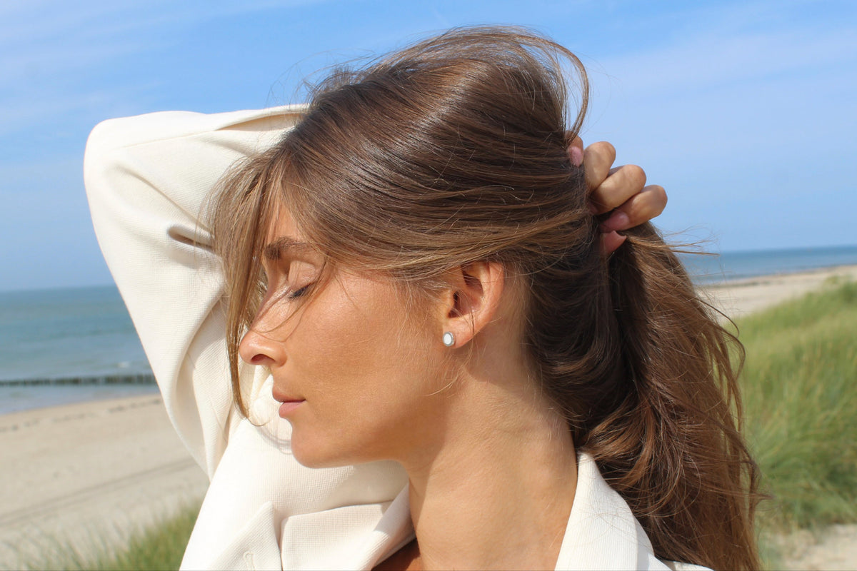 Woman in profile with eyes closed on a beach, wearing a silver Circle of Life breast milk stud